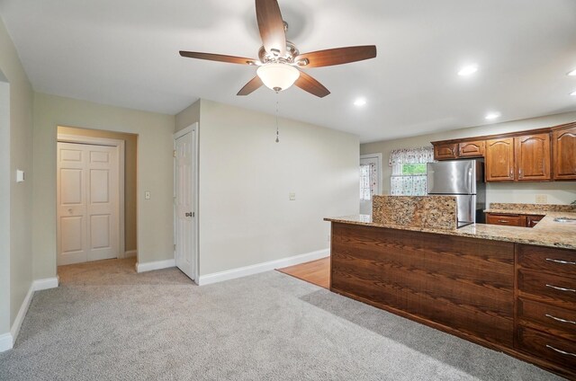 kitchen with freestanding refrigerator, a ceiling fan, light stone countertops, light colored carpet, and recessed lighting