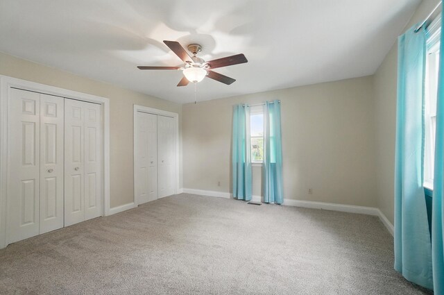 unfurnished bedroom featuring multiple closets, carpet floors, ceiling fan, and baseboards