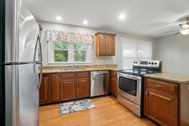 kitchen with stainless steel appliances, a sink, a peninsula, light stone countertops, and light wood finished floors