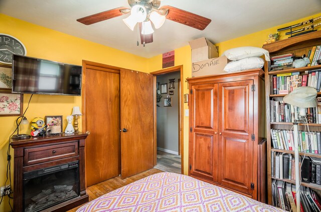 bedroom featuring a fireplace, a ceiling fan, and wood finished floors