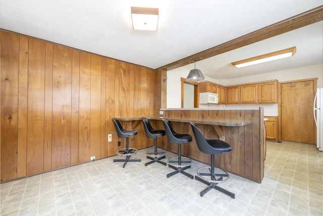 312 E Buckeye St, Belle Center, OH 43310 - kitchen with white appliances, light flooring, brown cabinetry, a kitchen bar, and wooden walls