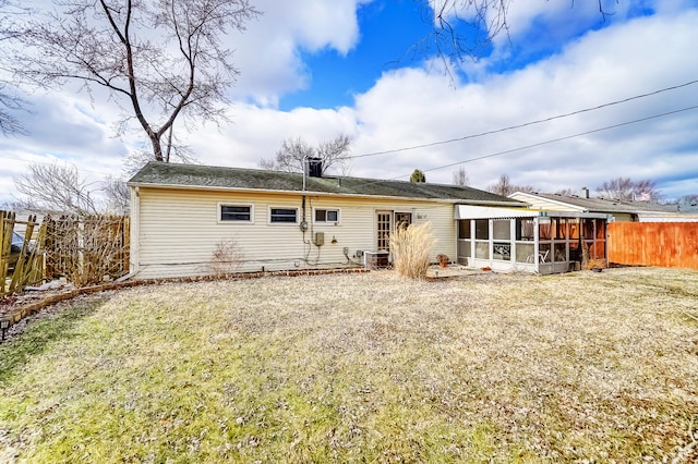 rear view of property featuring a sunroom, fence, and a lawn