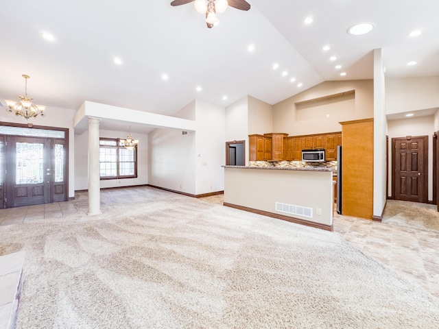 unfurnished living room featuring high vaulted ceiling, ceiling fan with notable chandelier, light carpet, visible vents, and ornate columns