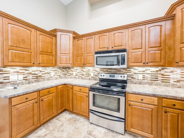 kitchen featuring light stone counters, backsplash, stone finish flooring, brown cabinetry, and appliances with stainless steel finishes