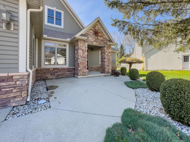 view of front of house with a patio area, stone siding, and a shingled roof