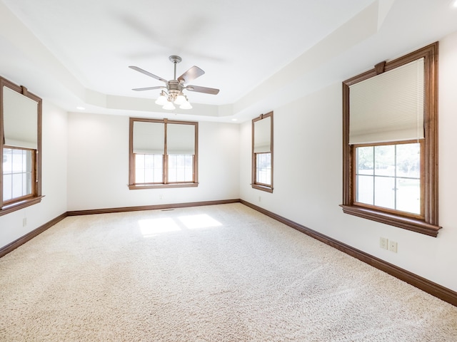 carpeted empty room with baseboards, a ceiling fan, a tray ceiling, and plenty of natural light