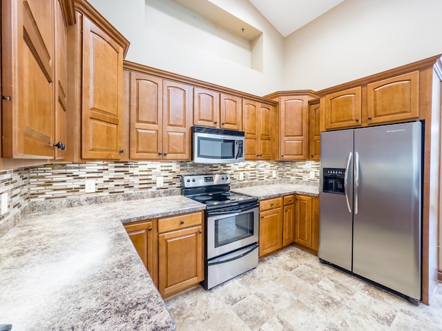 kitchen featuring a towering ceiling, backsplash, stone finish flooring, brown cabinets, and appliances with stainless steel finishes