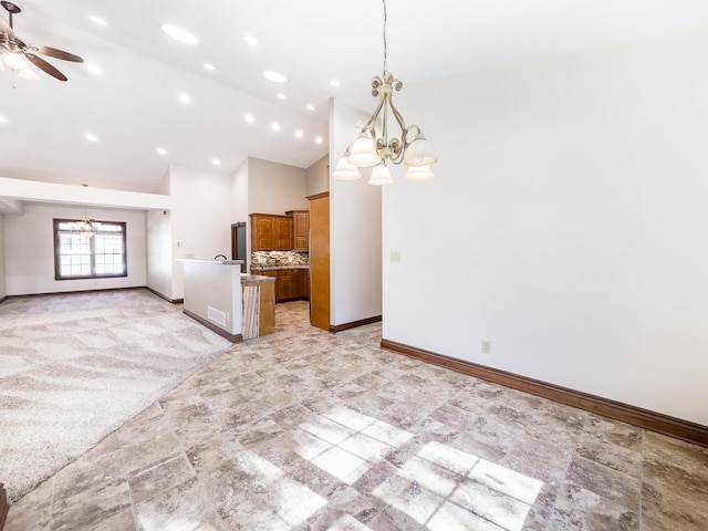 empty room featuring high vaulted ceiling, ceiling fan with notable chandelier, stone finish flooring, baseboards, and visible vents