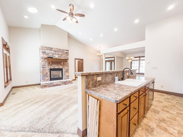 kitchen featuring a kitchen island with sink, a sink, ceiling fan with notable chandelier, brown cabinetry, and a stone fireplace