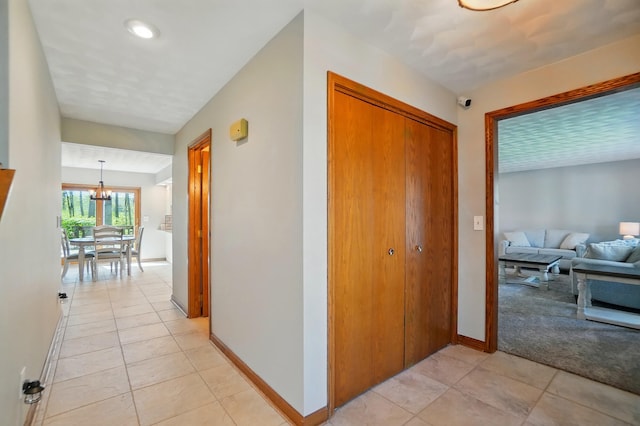 hall with baseboards, recessed lighting, light tile patterned floors, and a notable chandelier