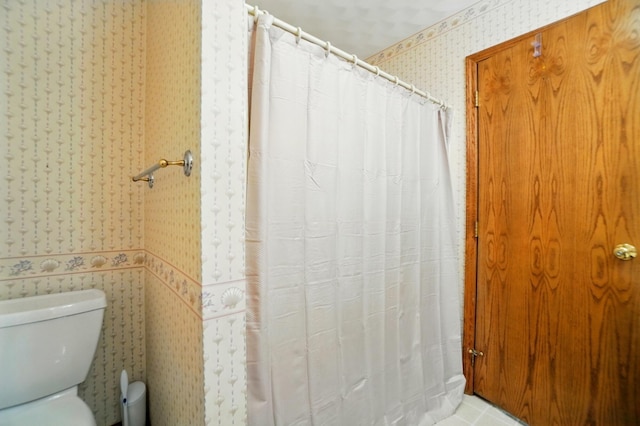 bathroom with a shower with curtain, toilet, and wallpapered walls