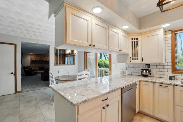 kitchen with light stone counters, a peninsula, backsplash, stainless steel dishwasher, and glass insert cabinets