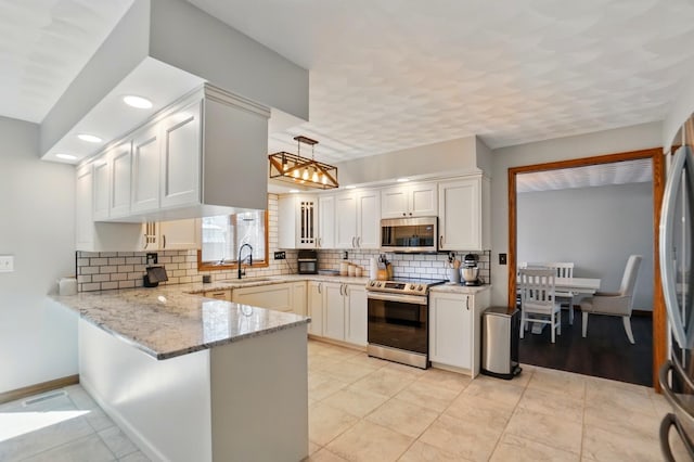 kitchen featuring decorative backsplash, light stone countertops, a sink, a peninsula, and stainless steel appliances