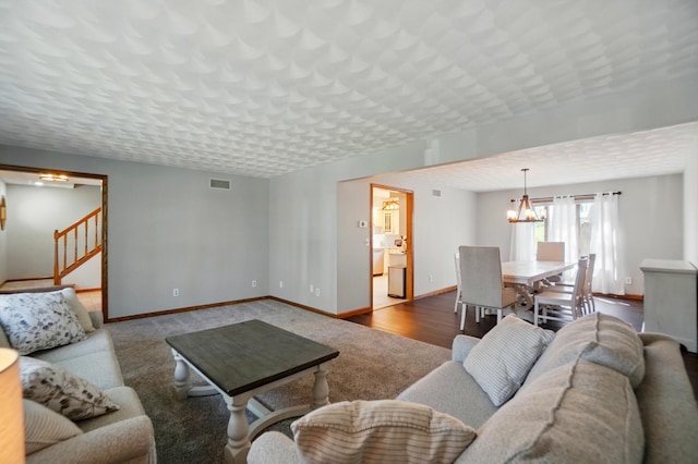 carpeted living area featuring baseboards, a chandelier, and stairway