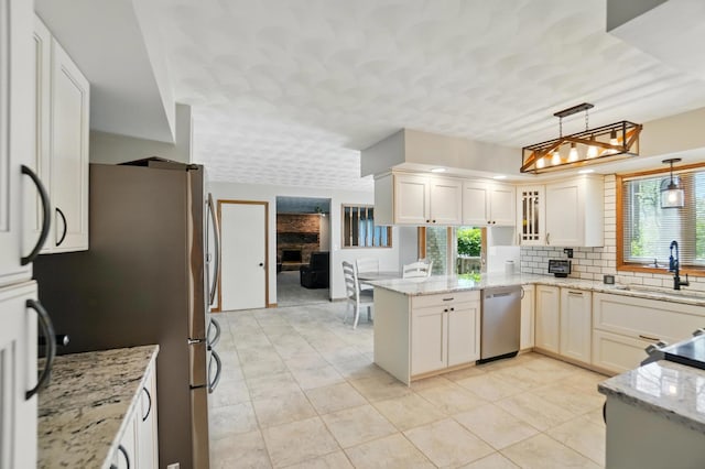 kitchen featuring pendant lighting, a peninsula, tasteful backsplash, a sink, and stainless steel appliances