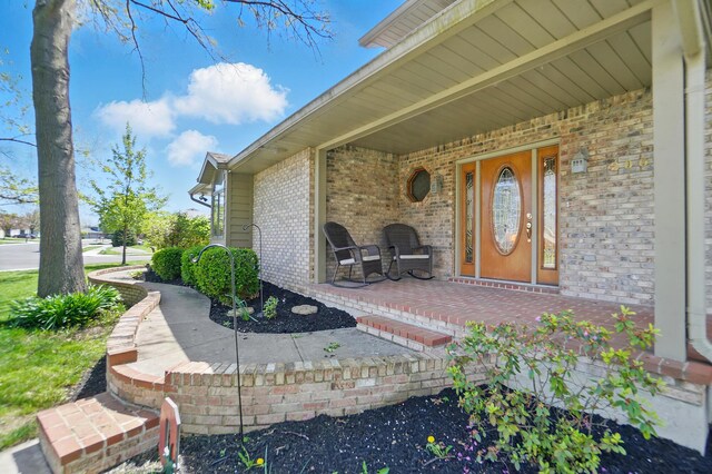 doorway to property with a porch and brick siding