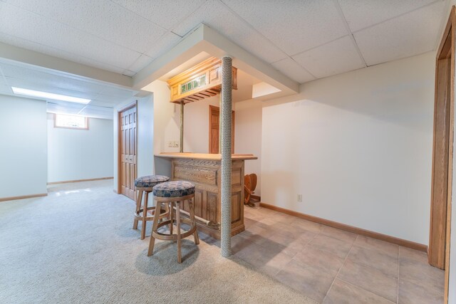 bar featuring a paneled ceiling, a bar, and baseboards