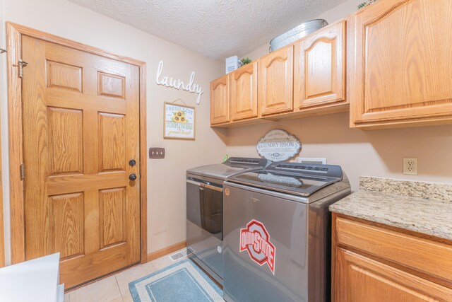 clothes washing area with a textured ceiling, baseboards, cabinet space, washer and dryer, and light tile patterned floors