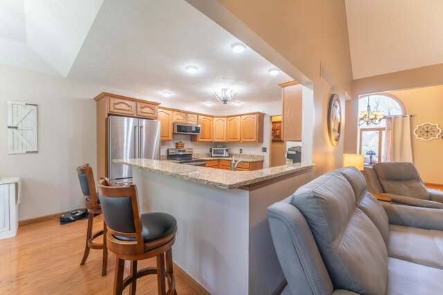 kitchen featuring stainless steel appliances, light wood-type flooring, light stone countertops, a kitchen bar, and open floor plan