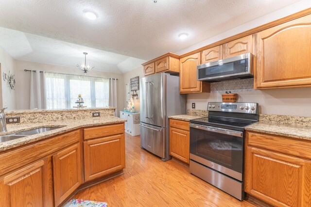 kitchen with light stone counters, a sink, light wood-style floors, and appliances with stainless steel finishes