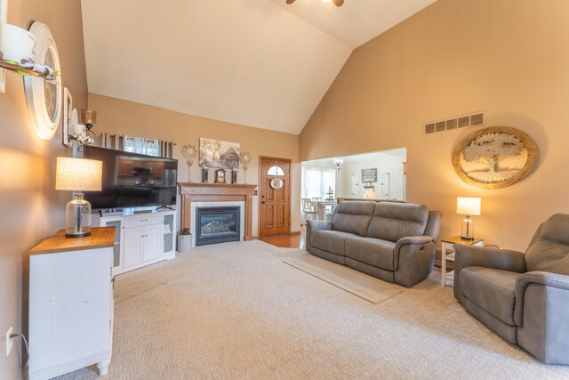 living room featuring light carpet, visible vents, a ceiling fan, a tile fireplace, and high vaulted ceiling