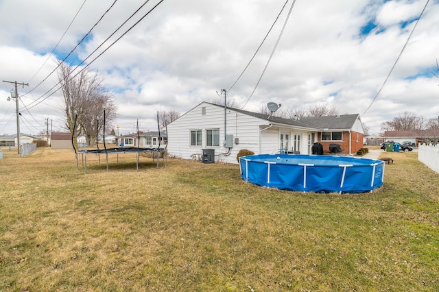 rear view of property with a lawn, a trampoline, cooling unit, and a fenced in pool