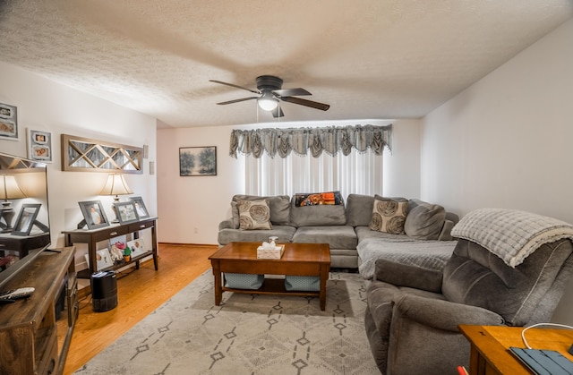 living area featuring a ceiling fan, a textured ceiling, baseboards, and wood finished floors