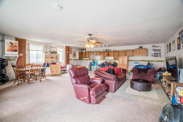 living area featuring ceiling fan, attic access, and light colored carpet