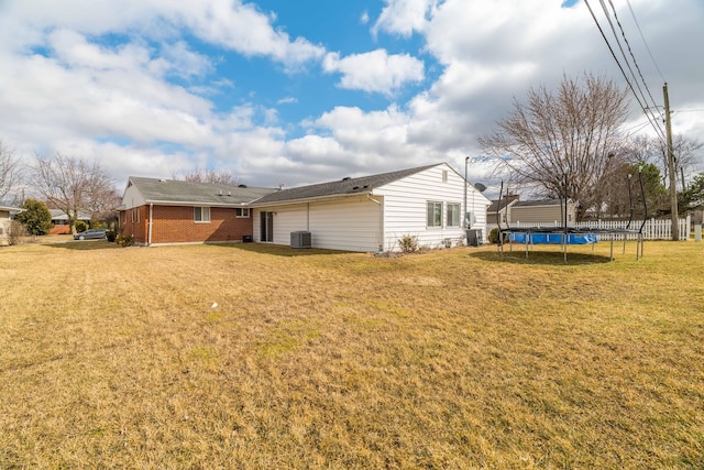 exterior space featuring a yard, brick siding, a trampoline, and central air condition unit