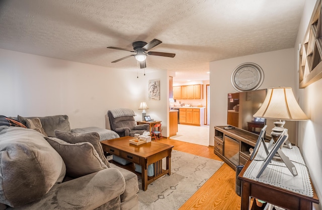 living room featuring light wood finished floors, ceiling fan, and a textured ceiling