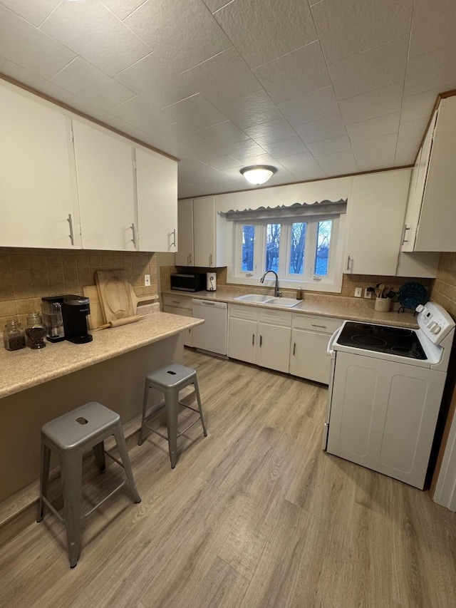 kitchen featuring sink, a breakfast bar area, white cabinetry, light wood-type flooring, and white appliances