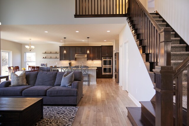 living area with light wood-style floors, recessed lighting, a chandelier, and stairway