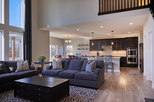 living room featuring a notable chandelier, a high ceiling, recessed lighting, and light wood-type flooring
