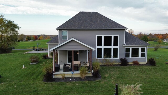 back of property with a lawn, a shingled roof, and a patio