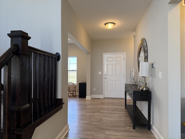 entryway featuring light wood finished floors, baseboards, and a textured ceiling