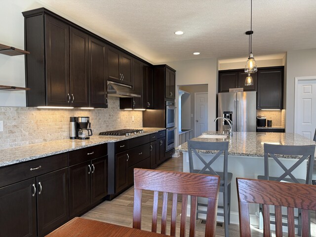 kitchen with open shelves, light wood finished floors, a kitchen breakfast bar, under cabinet range hood, and stainless steel appliances