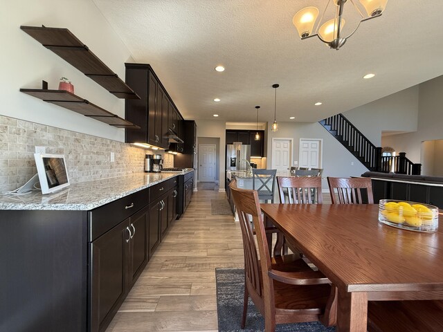 dining room featuring a textured ceiling, light wood-style flooring, recessed lighting, stairway, and an inviting chandelier