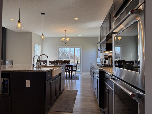 kitchen featuring dark stone counters, stainless steel appliances, dark wood-type flooring, a sink, and an inviting chandelier