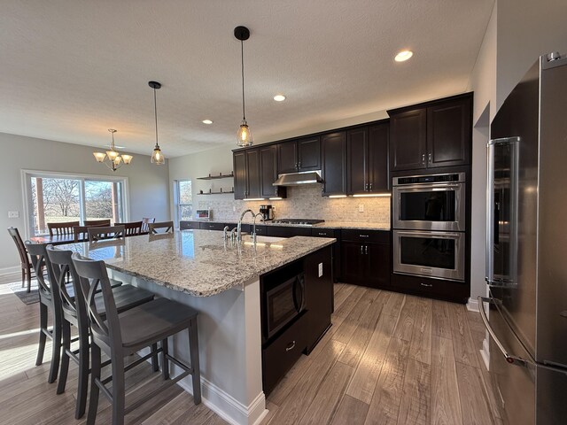 kitchen with decorative backsplash, a chandelier, appliances with stainless steel finishes, a sink, and a kitchen breakfast bar
