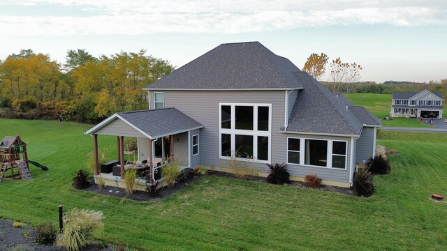 back of property featuring a lawn, a playground, and roof with shingles