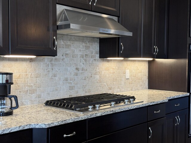 kitchen with stainless steel gas cooktop, under cabinet range hood, light stone counters, and tasteful backsplash