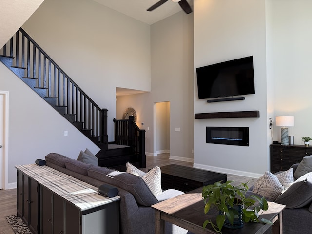 living room featuring stairs, wood finished floors, a glass covered fireplace, and a ceiling fan