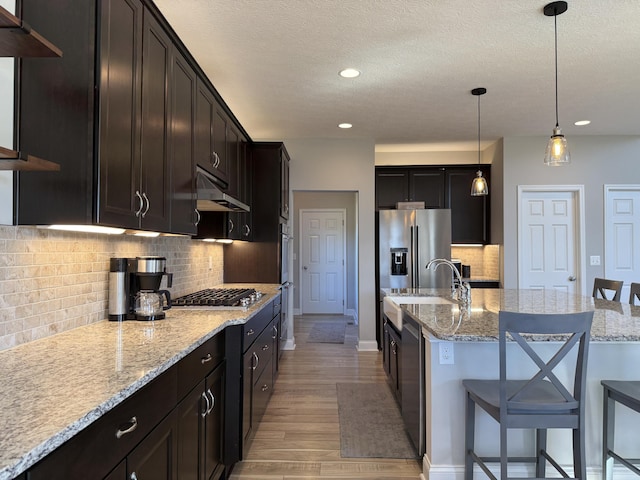 kitchen with a sink, a breakfast bar area, appliances with stainless steel finishes, light wood-style flooring, and under cabinet range hood