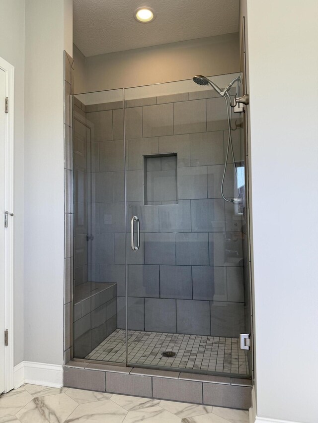 bathroom with marble finish floor, baseboards, and a shower stall
