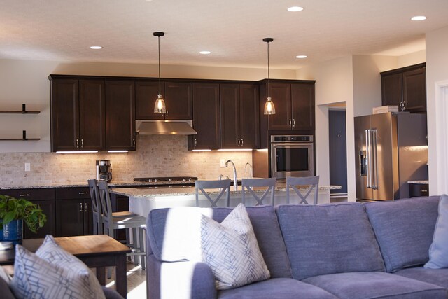 kitchen featuring open floor plan, dark brown cabinets, stainless steel appliances, and under cabinet range hood