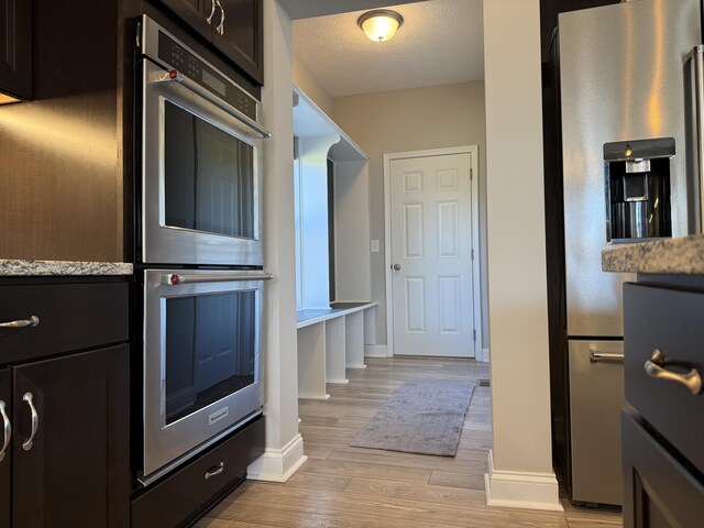kitchen featuring light stone counters, light wood finished floors, appliances with stainless steel finishes, a textured ceiling, and baseboards