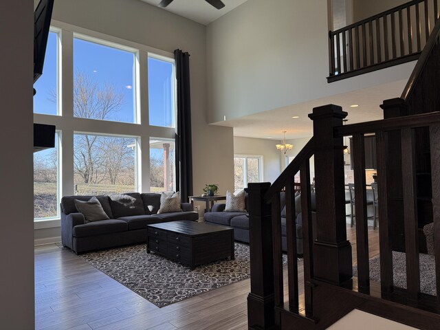 living room featuring ceiling fan with notable chandelier, wood finished floors, and a towering ceiling