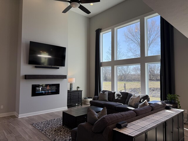 living room featuring dark wood-style flooring, a towering ceiling, a glass covered fireplace, and baseboards