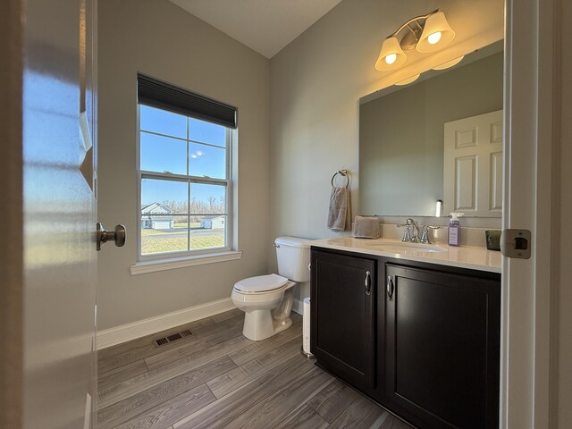 bathroom with toilet, vanity, wood finished floors, baseboards, and visible vents