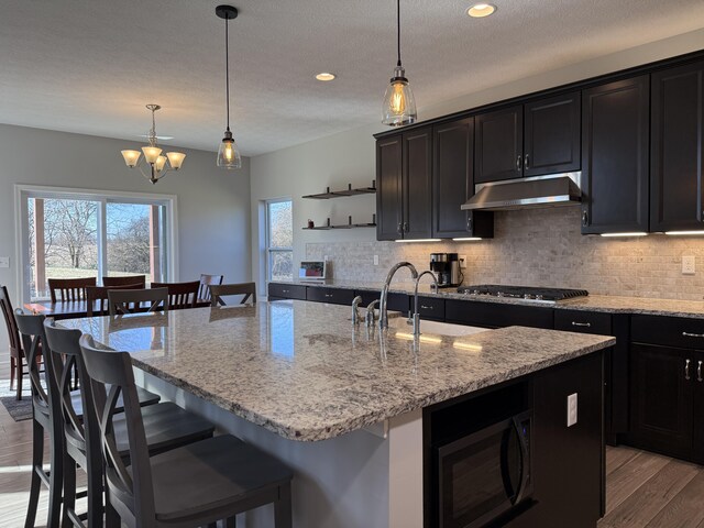 kitchen featuring tasteful backsplash, open shelves, light wood-type flooring, under cabinet range hood, and stainless steel gas stovetop